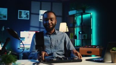 Dj 'i çeken sanatçı stüdyo stüdyosunda özel ders hazırlıyor, izleyicilere ses kontrol cihazından örnekler gösteriyor. Çevrimiçi yıldız oturma odasındaki abonelere modern müzik ekipmanlarını gösteriyor