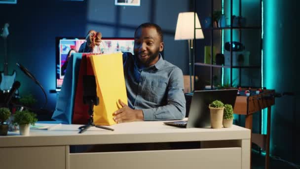 非裔美国人内容创作者拿着购物袋 在私人家庭工作室里拍摄视频 媒体明星打开他买的衣服 查看时装店的商品 — 图库视频影像