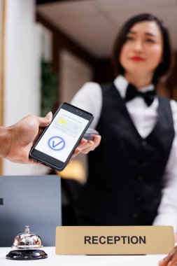 Cep telefonuyla ödeme yapan ve Po Terminali 'nde NFC' de çalışan bir adam, kontrol eden insanlara yardım eden bir resepsiyonist. Asyalı resepsiyon görevlileri misafirleri karşılıyor, yetişkinler oda için ödeme yapıyor. Kapat..