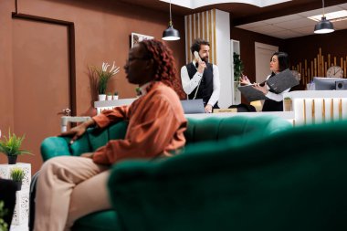 Otel çalışanları rezervasyonların kaydını tutuyor, telefon görüşmelerini cevaplıyor ve online oda rezervasyonlarını not ediyor. Çeşitli işçiler misafirleri karşılıyor ve resepsiyondaki dosyaları inceliyor..