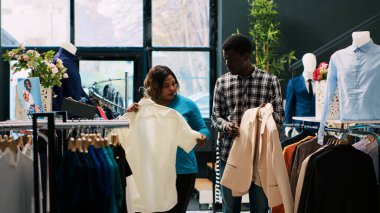 Modern butikte gündelik kıyafet alışverişi yapan Afro-Amerikalı bir çift. Neşeli müşteriler kıyafet malzemelerini kontrol ediyor, yeni gardırop için şık ürünler alıyor. Moda.