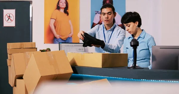 Diverse workers discussing shipping details in modern boutique, preparing packages for delivery. Employees working at customers orders, putting fashionable clothes in carton boxes in shopping centre