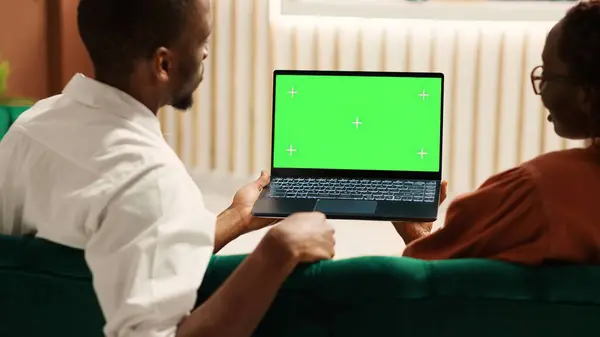 Bored tourists watching video on laptop chroma key green screen mock up waiting for check in process to be over. Guests sitting in hotel foyer while porter employee carries luggage to their room