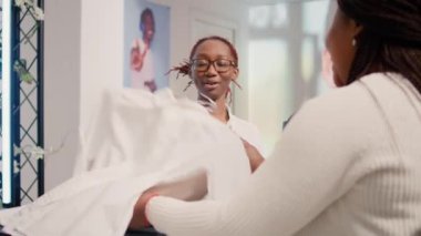 Afro-amerikan kasiyer şık giyim mağazasında sırada bekleyen müşteriler için kasiyer ürünleri işliyor. Çalışan müşterilere alışverişlerinde yardımcı olur, çekimler yaparlar.