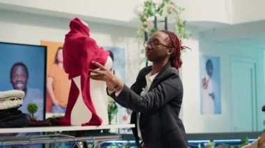 Lüks moda butiğinde çalışan titiz perakende asistanı, mankenin üzerine kadın bluzu giyiyor. Deneyimli Afro-Amerikan çalışanı yeni moda giysiler koleksiyonunu sergiliyor.