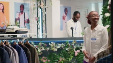 Perakendeciler müşterilerine şık moda mağazalarında şık kıyafetler bulmalarında yardımcı olurlar. Dost canlısı işçi, müşteriye seçkin tasarımcı erkek gömlekleri koleksiyonu bulması için yardımcı oluyor.