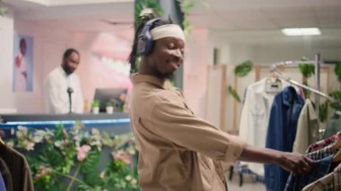 Giyim mağazasında müzik dinleyen ve dans eden bir adam, malzemelerin niteliksel olup olmadığını belirlemeye çalışıyor. Müşteriler kıyafetleri incelerken moda butiği yapıyorlar.