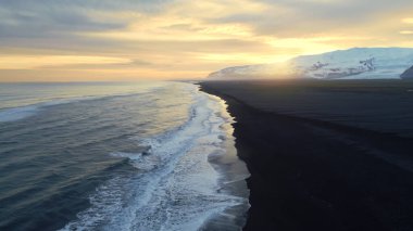 Nordik okyanus kıyılarının doğal siyah kumlu sahili, İzlanda manzarası, karlı dağlar ve tarlaları. Yol kenarındaki görkemli altantik kıyı şeridi, kutup panoramik manzarası. Yavaş çekim.