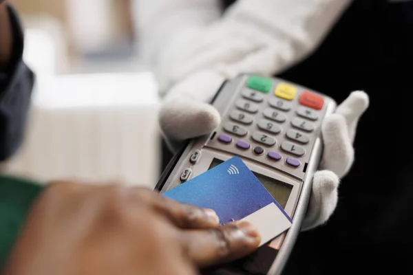 Close up of hotel guest paying for room at front desk, male hand holding plastic credit card making contactless payment. Cashless transactions and nfc technology in hospitality industry