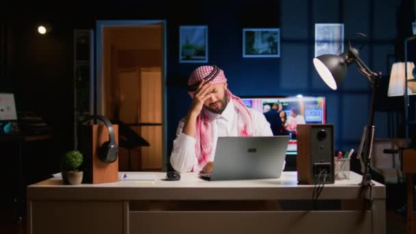 疲れたアラブのビジネスマンは 自宅のオフィスで働く片頭痛に苦しんでいます リビングルームで疲れ果てた中東の従業員は 過労から頭痛を得る電子メールに答えます — ストック動画