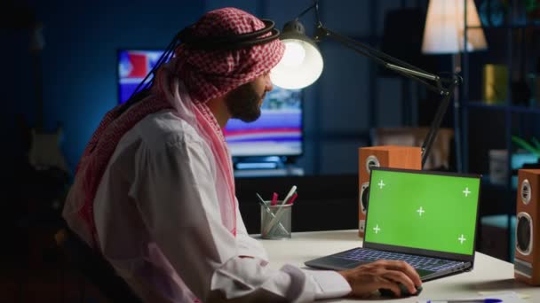 在家里工作的时候 阿拉伯人在电脑上浏览 自营职业的自由职业者在以电视为背景噪音的公寓办公室的隔离屏幕设备上查看电子邮件 — 图库视频影像