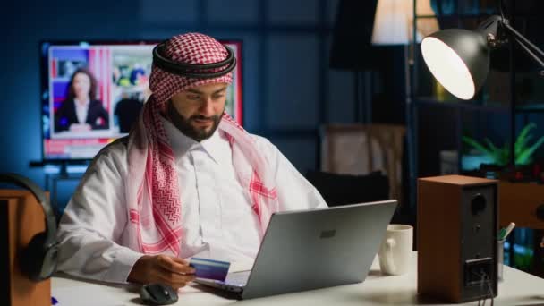 オンラインショッピングをするアラビア人男性は 慎重にコンピュータ上のクレジットカード情報を入力します ムスリムの人は 夜に居心地の良いスタイリッシュな暖かい家で ウェブサイト上で支払い方法を追加します — ストック動画
