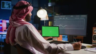 Daire ofisindeki Müslüman işçi bilgisayardaki iş yıllık rapor grafiklerine bakarken krom anahtar tablet tutuyor. Elinin altında dijital cihaz ile profesyonel serbest meslek görevleri yapıyor.