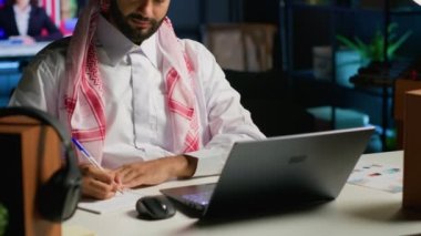 Ev ofisinin bilgisayarında çalışan Arap girişimci internete göz atıyor ve deftere yazı yazıyor. Müslüman adam telgraf çekerken kalem, not defteri ve dijital aygıt kullanıyor