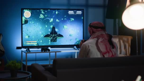 アラブのゲーマーは テレビでアーケード宇宙シューティングゲームをプレイした後に興奮しています ゲームシステムで自宅で時間を過ごす男 最終的にシングルプレイヤーのビデオゲームミッションを完了することに満足 — ストック動画