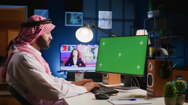 家で働いている間 クロマのキー コンピューター スクリーンを見るアラビアの男 自己はキーボードでタイプする人を雇用しましたり 背景騒音としてTvが付いているアパートのオフィスの緑のスクリーン デバイスの電子メールを送ります — ストック動画