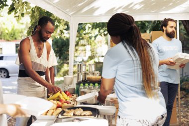 Çok kültürlü gönüllüler, gönüllü olma ve topluma yardım etme ruhunu somutlaştıran bir yemek kampanyasında sıcak yemek servisi yapmak için bir araya geliyorlar. Afro-Amerikalı evsiz adam bağışlanmış meyve alıyor..