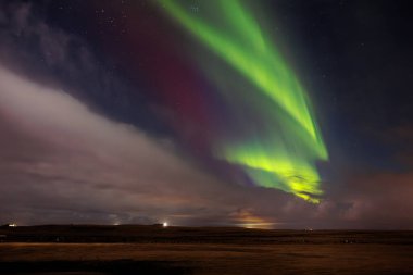 Kış mevsiminde karla kaplı yamaçtaki Aurora Borealis. İzlanda kuzey ışıkları, buzlu bir arazide gece gökyüzünü aydınlatan doğanın muhteşem bir görüntüsüdür..