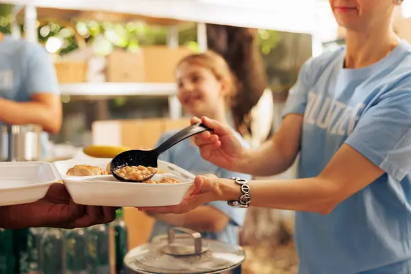 Close-up shot of caucasian charity worker providing fresh warm meal from an outdoor food bank to a person in need. Detailed view of free food being provided to the hungry and less fortunate.