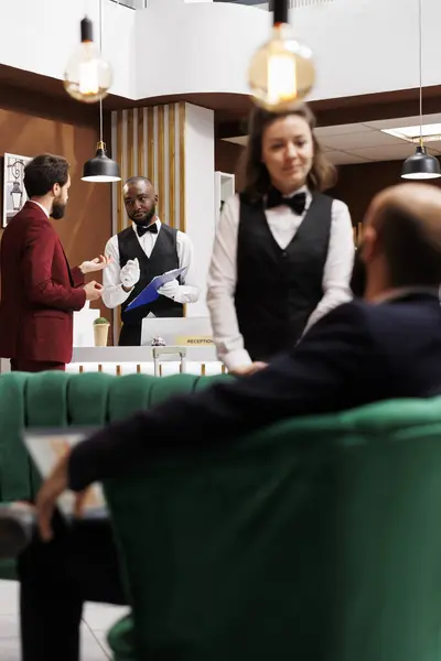 Businessman providing necessary information for receptionist, ensuring seamless check in procedure. Diverse people talking about local recommendation, guest travel on business trip.