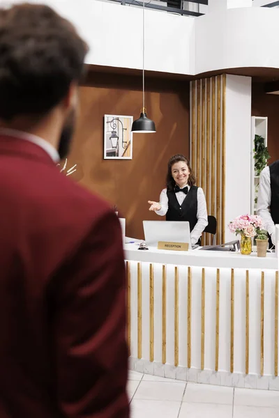 Employee welcoming businessman in lobby, providing luxury services for guest travelling on work trip. Guest arriving at resort with baggage, receiving friendly assistance from hotel staff.