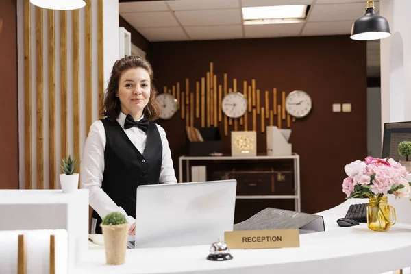 Friendly receptionist at front desk prepared to greet guests in hotel lobby, providing excellent customer services to ensure pleasant stay. Concierge working at reception, welcome people.
