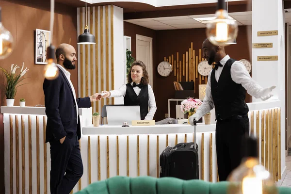 Businessman receives access card in hotel lobby, front desk diverse staff providing luxury services for guest upon his arrival. White collar worker being welcomed at resort, business trip.
