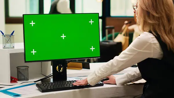 Front desk staff using greenscreen on pc in resort lobby, checking chroma key display with isolated template. Hotel receptionist looking at blank copyspace on computer. Tripod shot.