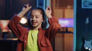 Küçük bir kızın sosyal medya platformu için büyüleyici dans hareketleri yaparken, viral bir meydan okuma yaparken yakın plan çekimi. Sevimli küçük çocuk çevrimiçi hayranları için loş ışıklı ev stüdyosunda video kaydediyor.
