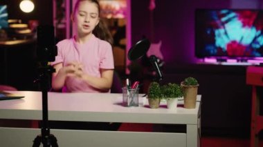 Genç kız çevrimiçi hayranları için içeriği filme alıyor, Z jenerasyonundan bahsediyor. Stüdyoda aile kanalı için arka planda pembe neon ışıkları olan şirin çocuk video bloğu kaydediyor.