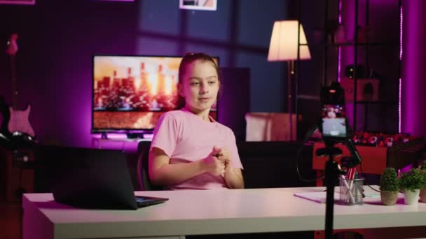 Gen Zの子供がオンラインチャンネルで撮影し 視聴者と話すために使用するレコーディング技術 若い聴衆とのトピックを議論するネオンリビングルームで幸せな子供 スマートフォンで映像をキャプチャ — ストック動画