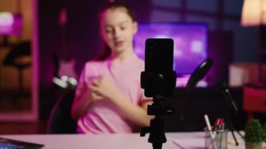 Profesyonel stüdyo olarak kullanılan pembe neon ışıklı oturma odasında tripod dengeleyicisiyle akıllı telefonla çekim yapan çocuk. Neşeli kız cep telefonu kamerasıyla okuldaki eğlenceli günlerden bahsederken görüntüler yakalıyor.