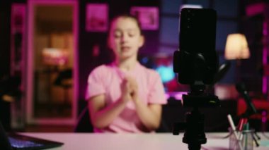 Akıllı telefondan yakın çekim. Tripodla, enerjik genç bir kızın kendini videoya çekişini, çocukların onu izlemesi için ilgi alanlarını tartışmasını, çevrimiçi sosyal medya içeriğini kaydetmesini.