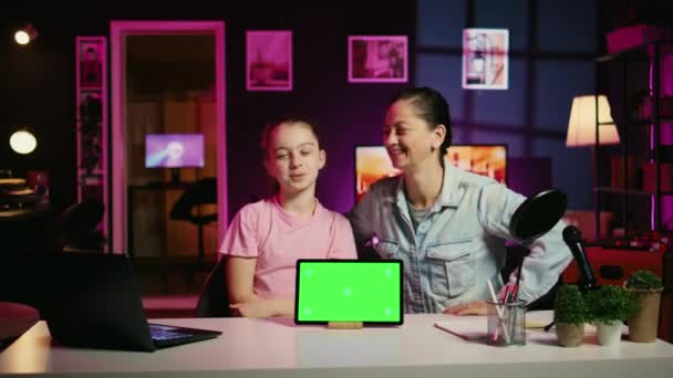 スポンサーブランドのグリーンスクリーンタブレットを使用して 彼女の親とオンラインコンテンツを撮影する笑顔の娘 幸せな子供と彼女の母親は クロマキーデバイスを使用してファンのためのインターネットビデオを行う — ストック動画
