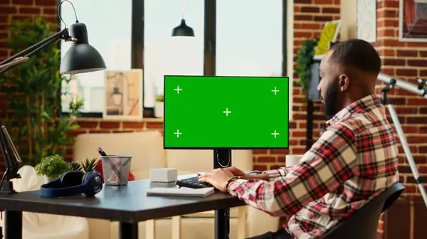 在公寓客厅里 非裔美国人远程工作自由职业者在彩色键上输入数据 模拟计算机绿色屏幕 在家工作时执行任务的远程雇员松懈 — 图库照片