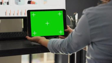 İş kadını, başlangıç ajansının ortak çalışma alanındaki tablet üzerinde yeşil ekran kullanır, cihaz ekranındaki telif alanı modelleme şablonuna bakar. Uzman masadaki kromakey görüntüsünü kontrol ediyor.