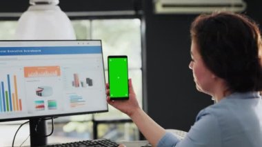 Uzay iş merkezindeki yeşil ekranlı telefonu elinde tutan yönetici, boş model ekranlı mobil cihaza bakıyor. Uzman, izole edilmiş telif alanı düzenini kontrol ediyor. El kamerasıyla..