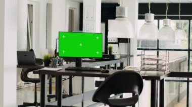Çalışma masasında çalışan yeşil ekran monitörü, açık kat planı küçük işletme ofisi. Bilgisayar boş kromakey ekranlı, modern kariyerli izole bir model şablonu gösteriyor.
