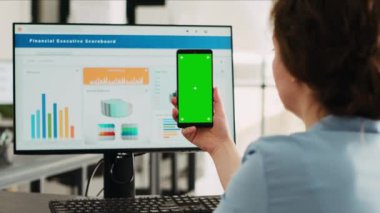 İş kadını telefonda yeşil ekranı tutuyor ve büro masasında pazarlama geliştirme üzerinde çalışıyor. Ekranda model kromakey şablonu ve izole edilmiş telif alanı kullanan şirket çalışanı.