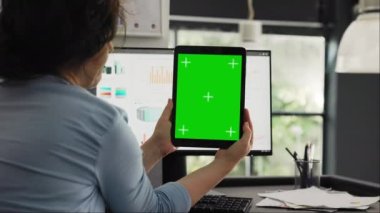 İş kadını elinde tablet tutarak izole edilmiş yeşil ekran şablonu sunuyor, modern aygıttaki boş kopyalama alanına bakıyor. Gadget düzeninde çalışan Chromakey tasarımı denetleniyor.