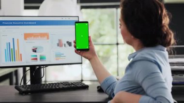 Çalışan masasında cep telefonu tutuyor, akıllı telefon cihazında sunulan izole edilmiş yeşil ekran düzenine bakıyor. Modern yazılım teknolojisi ile çalışan iş kadını, kromakey modeli.