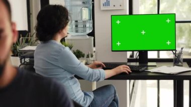 Ofis çalışanı çalışma istasyonundaki yeşil ekrana bakar, izole edilmiş kromakey ekranı kontrol eder. Bilgi yazan ve boş masayı inceleyen kadın.
