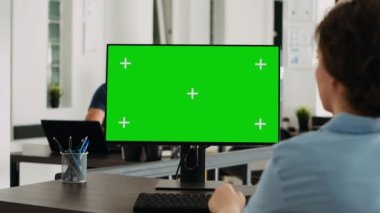 Çalışma istasyonundaki bilgisayarda izole edilmiş yeşil ekran ile çalışan yönetici, masasında model şablonu olan kromakey ekrana bakıyor. İş kadını ortak çalışma alanında bilgisayarı kullanıyor.