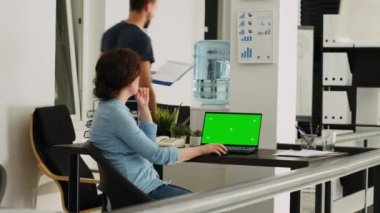 Ofis çalışanı masadaki küçük işletmeler üzerinde çalışırken dizüstü bilgisayarda yeşil ekran izliyor. İzole edilmiş kromakey şablonunu taklit boşluğu olan ekrana bakan kişi.