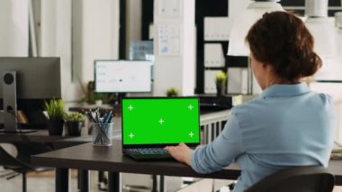 Ofisteki iş işleri ve işlemleri çözmek için yeşil ekranlı dizüstü bilgisayar kullanan bir uzman, ortak çalışma alanındaki kromakey ekrana bakıyor. Kopyalama alanı ile kablosuz bilgisayar üzerinde çalışan kadın.