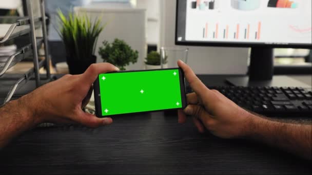 员工的Pov在办公桌前配备了绿色显示屏 在工作站上配备了独立的模拟模板 年轻员工看着带有铬钥匙的手机屏幕 — 图库视频影像