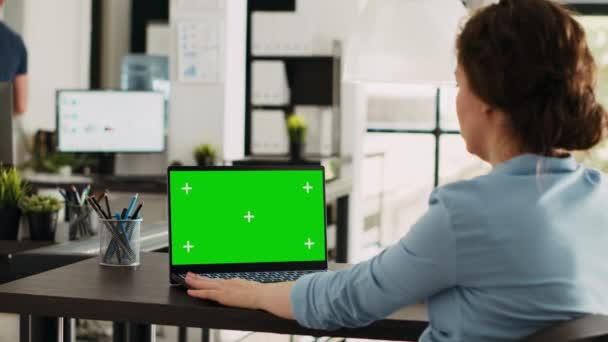 ラップトップのグリーンスクリーンでオフィスデスクで作業するマネージャー モックアップクロメイキーディスプレイと隔離されたコピースペーステンプレートを分析します ワークステーションでパソコンを使用する女性 — ストック動画
