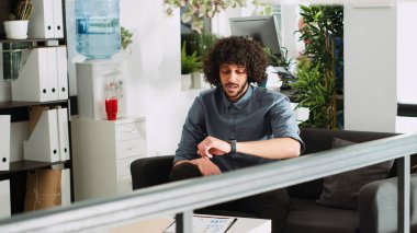 Analyst answering smartwatch call in small business office, talking to colleague about new investment strategy. Modern employee working with gadget for briefing remote meeting. Tripod shot.
