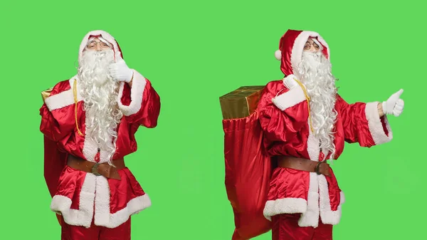 圣诞老人在镜头前竖起大拇指 在绿屏的背景下感到积极的奉献和同意的象征 圣诞老人西服表达对礼物袋的认可 — 图库照片