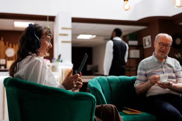 Senior Woman Headphones Sitting Sofa Hotel Lobby Confirming Reservation Device — Stock Photo, Image